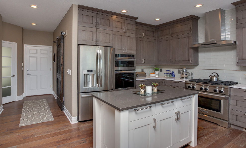 Eat-in kitchen - large transitional u-shaped medium tone wood floor eat-in kitchen idea in Denver with a farmhouse sink, shaker cabinets, gray cabinets, quartz countertops, gray backsplash, glass tile backsplash, stainless steel appliances and an island