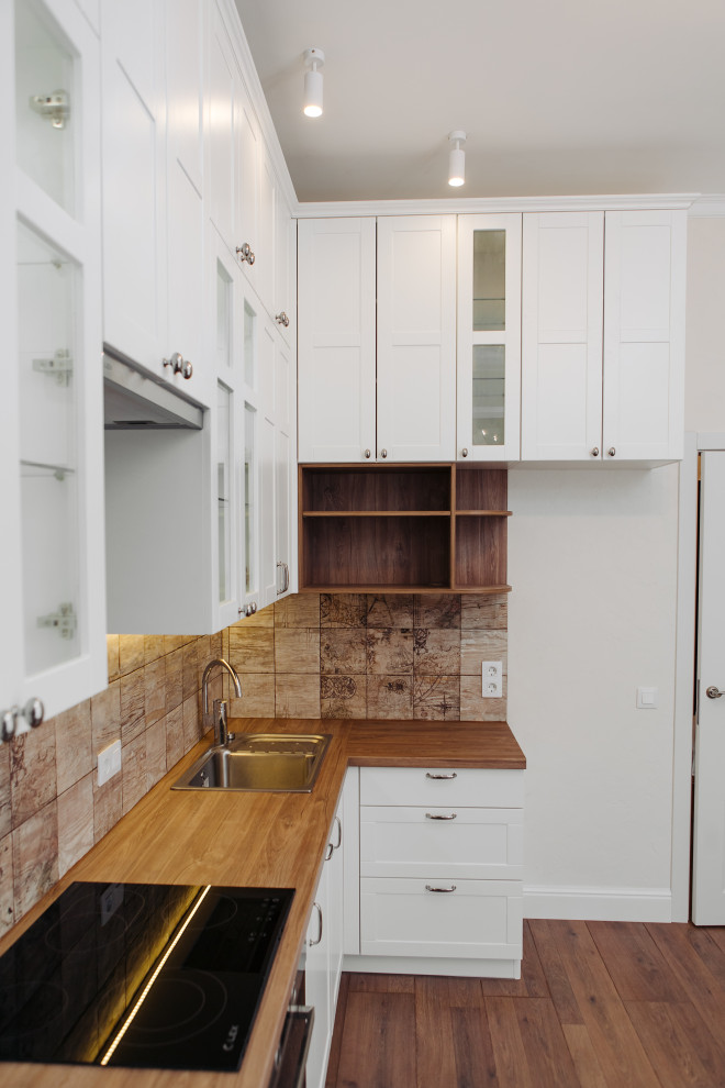 Photo of a medium sized scandinavian l-shaped enclosed kitchen in Saint Petersburg with a submerged sink, recessed-panel cabinets, white cabinets, laminate countertops, beige splashback, ceramic splashback, black appliances, laminate floors, no island, brown floors and brown worktops.