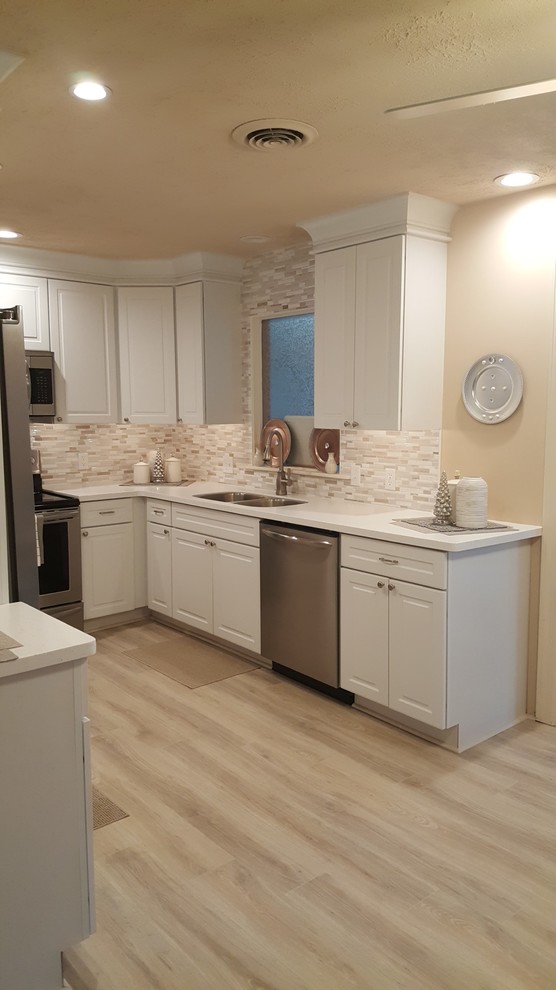 Example of a small l-shaped eat-in kitchen design with an undermount sink, raised-panel cabinets, white cabinets, quartz countertops, white backsplash, porcelain backsplash, stainless steel appliances and no island