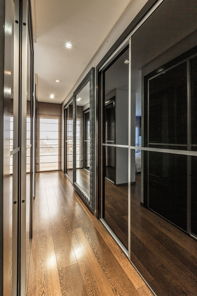 Photo of a contemporary gender-neutral dressing room in Other with glass-front cabinets, medium hardwood floors and brown floor.