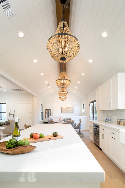 Mid-sized beach style l-shaped open plan kitchen in San Francisco with a farmhouse sink, shaker cabinets, white cabinets, quartz benchtops, white splashback, marble splashback, stainless steel appliances, light hardwood floors and with island.