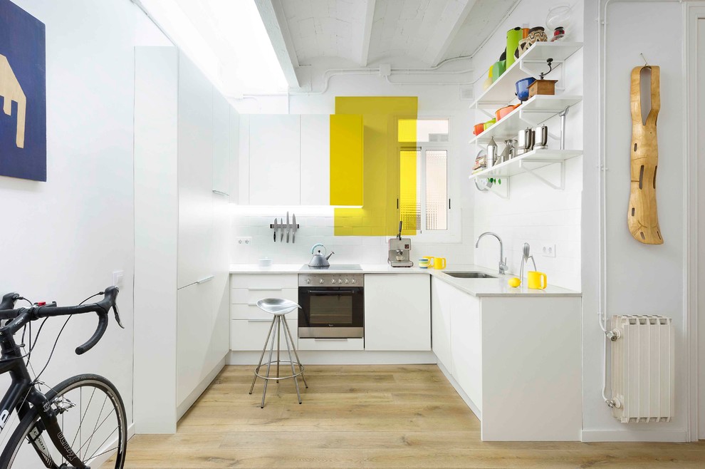 Inspiration for a small contemporary l-shaped open plan kitchen in Barcelona with a single-bowl sink, flat-panel cabinets, white cabinets, white splashback, ceramic splashback, stainless steel appliances, medium hardwood floors and no island.