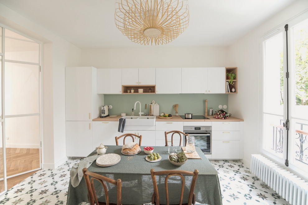 This is an example of a large single-wall kitchen in Paris with a double-bowl sink, white cabinets, wood benchtops, green splashback, cement tiles, no island and multi-coloured floor.