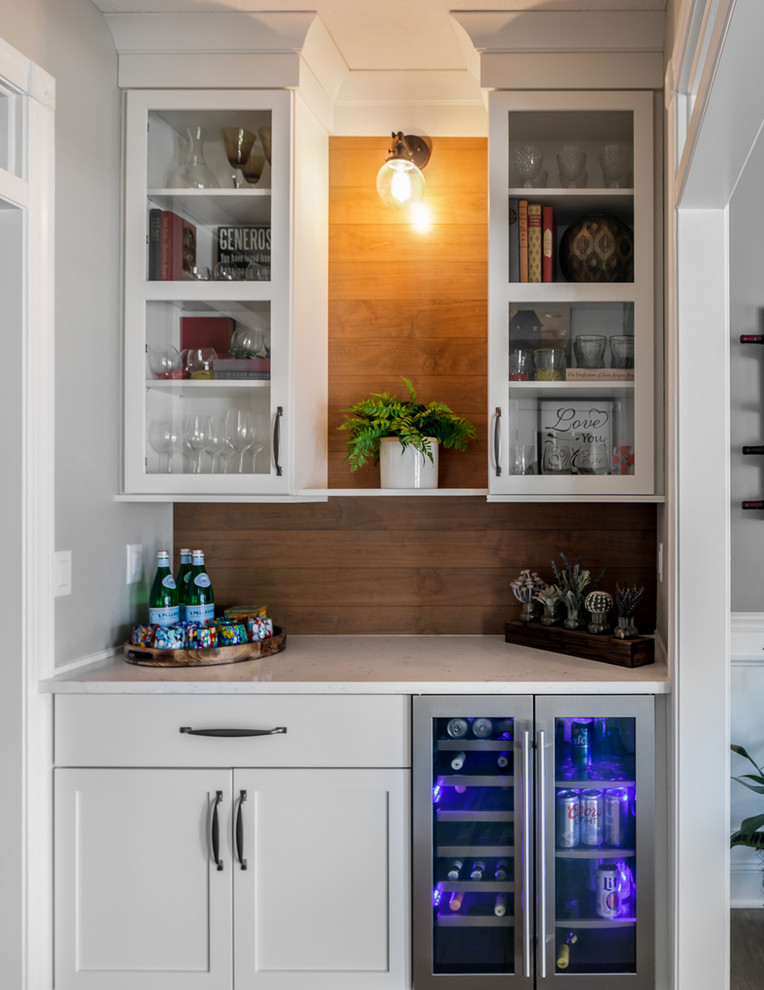 U-shaped brown floor eat-in kitchen photo with shaker cabinets, white cabinets, quartz countertops, white backsplash, subway tile backsplash, stainless steel appliances, an island, white countertops and a farmhouse sink