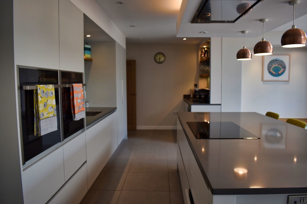 Design ideas for a large contemporary single-wall eat-in kitchen in Cambridgeshire with an undermount sink, flat-panel cabinets, grey cabinets, quartzite benchtops, brown splashback, glass tile splashback, black appliances, ceramic floors, a peninsula, grey floor and grey benchtop.