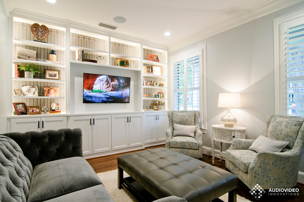 Photo of a mid-sized transitional enclosed living room in Dallas with a library, grey walls, medium hardwood floors, a wall-mounted tv and brown floor.