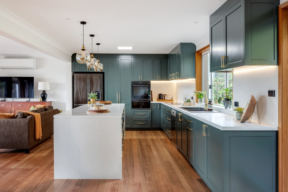 Large transitional l-shaped medium tone wood floor and multicolored floor eat-in kitchen photo in Sydney with a drop-in sink, shaker cabinets, green cabinets, quartz countertops, white backsplash, quartz backsplash, black appliances, an island and white countertops