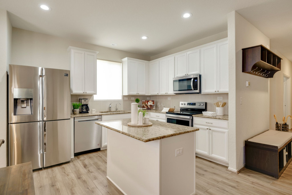 Kitchen - laminate floor and brown floor kitchen idea with an undermount sink, white cabinets, granite countertops, beige backsplash, stainless steel appliances and white countertops
