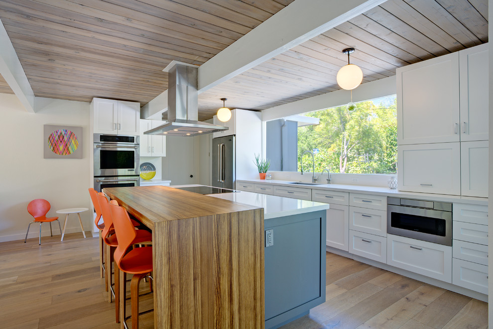 Photo of a midcentury open plan kitchen in San Francisco with an undermount sink, shaker cabinets, white cabinets, stainless steel appliances, light hardwood floors, with island and wood benchtops.