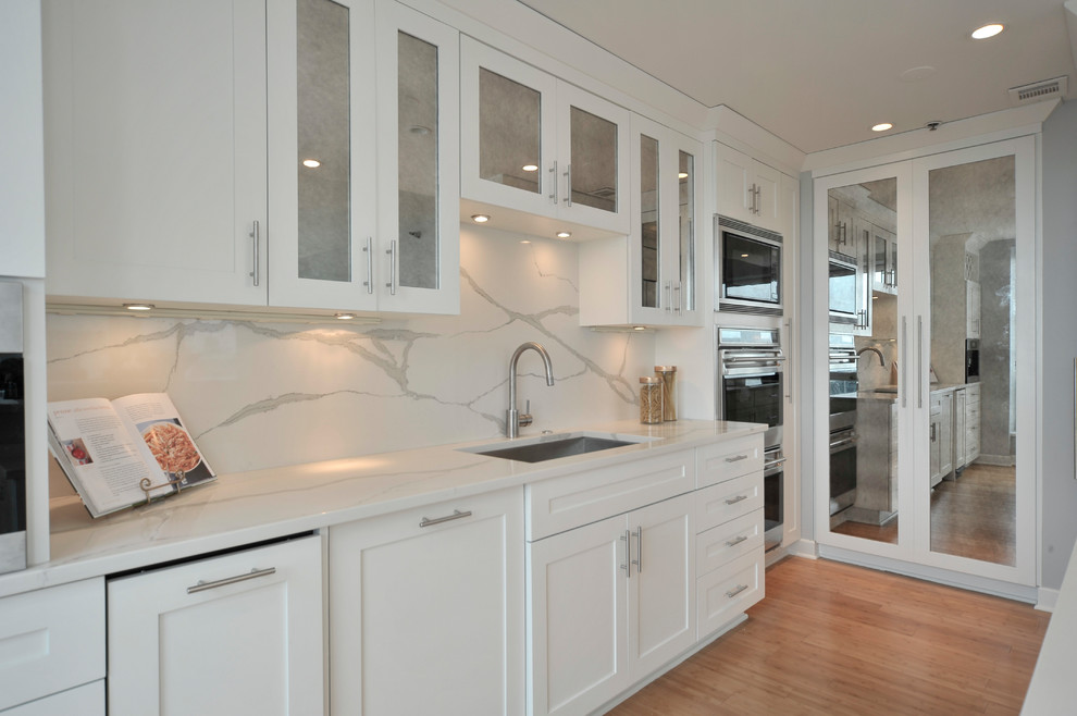 Inspiration for a small transitional galley bamboo floor eat-in kitchen remodel in Chicago with an undermount sink, flat-panel cabinets, white cabinets, quartzite countertops, white backsplash, stainless steel appliances and an island