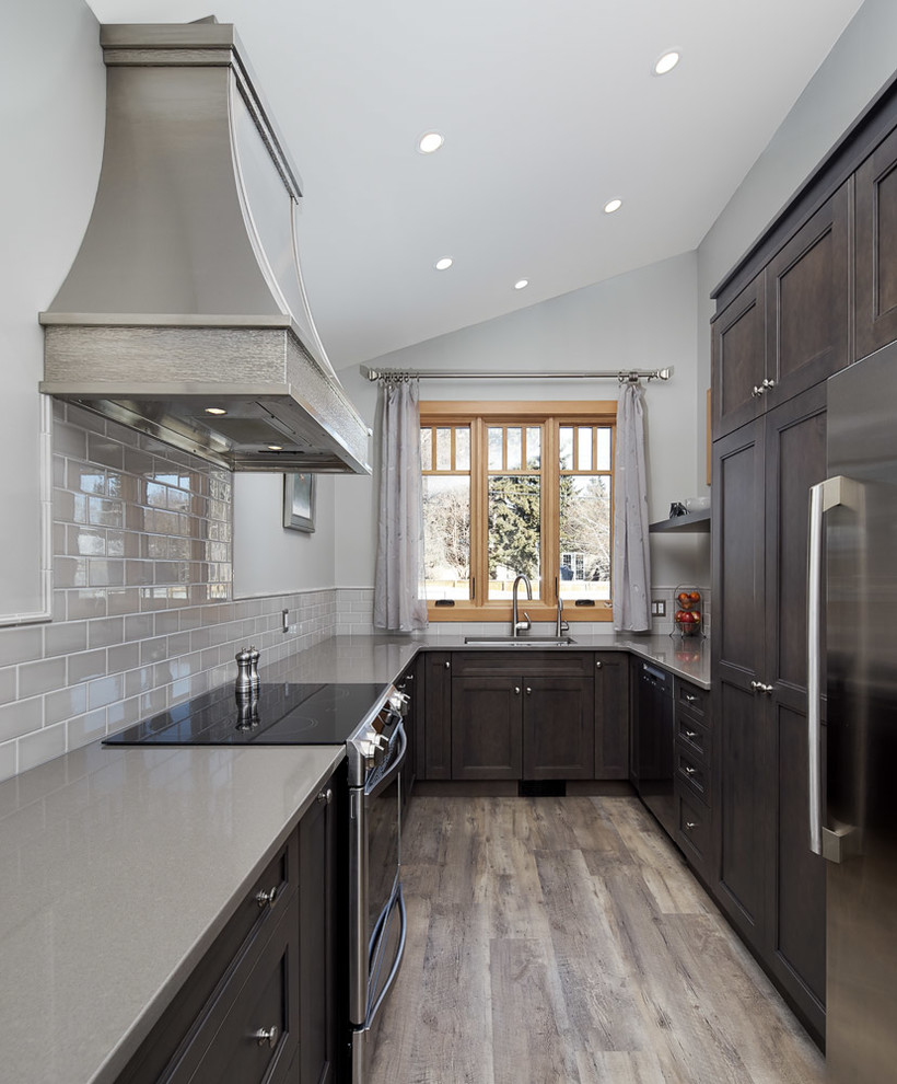 Inspiration for a small transitional u-shaped medium tone wood floor and gray floor open concept kitchen remodel in Calgary with an undermount sink, recessed-panel cabinets, dark wood cabinets, quartz countertops, gray backsplash, subway tile backsplash, stainless steel appliances and a peninsula