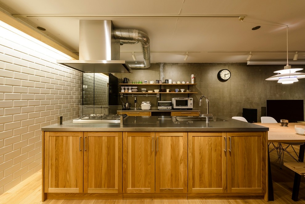 This is an example of an industrial single-wall kitchen in Fukuoka with a single-bowl sink, recessed-panel cabinets, medium wood cabinets, stainless steel benchtops, medium hardwood floors, with island and brown floor.
