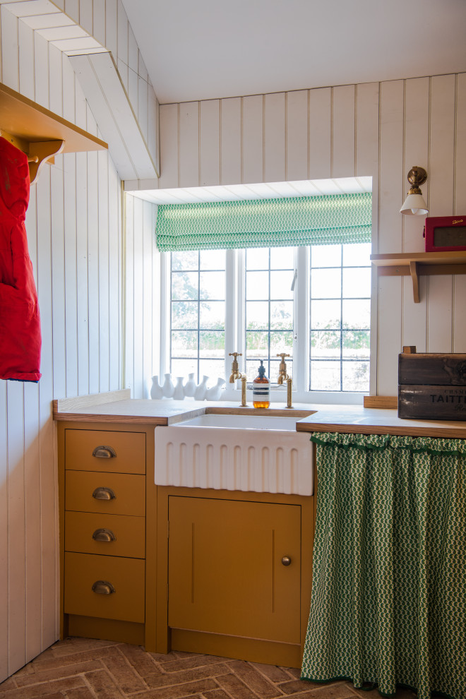 Esempio di una piccola lavanderia multiuso moderna con lavello stile country, ante a filo, ante gialle, top in legno, pareti bianche, pavimento in mattoni, pavimento marrone e top marrone