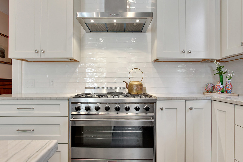 Design ideas for a large transitional l-shaped kitchen in New Orleans with an undermount sink, shaker cabinets, white cabinets, white splashback, stainless steel appliances, with island, quartzite benchtops, subway tile splashback, ceramic floors, brown floor and white benchtop.