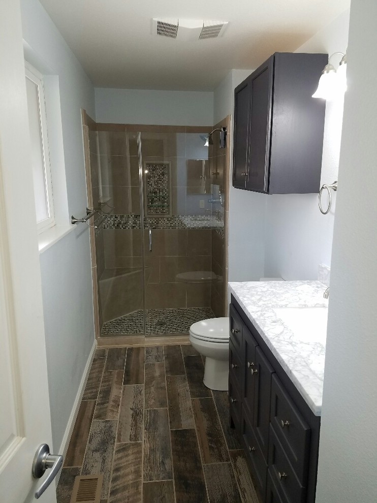Example of a mid-sized transitional beige tile and porcelain tile porcelain tile and beige floor alcove shower design with shaker cabinets, brown cabinets, a two-piece toilet, white walls, an undermount sink, granite countertops and a hinged shower door