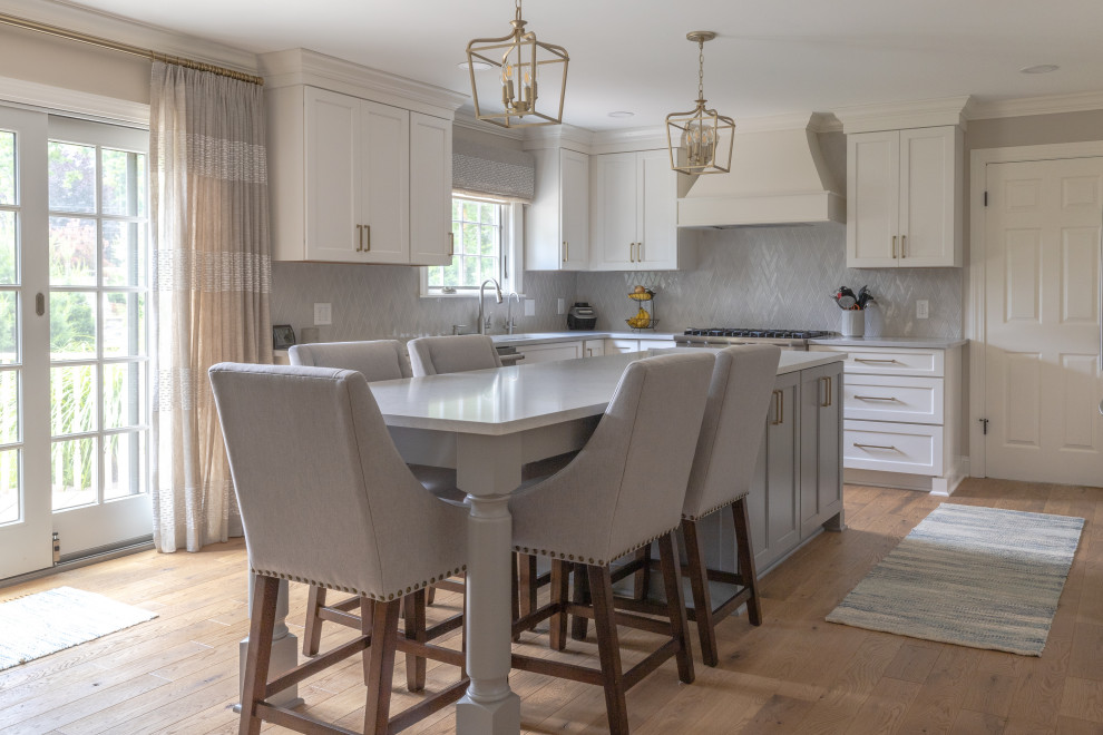 This is an example of a large transitional u-shaped eat-in kitchen in Detroit with an undermount sink, flat-panel cabinets, grey cabinets, quartz benchtops, grey splashback, mosaic tile splashback, stainless steel appliances, medium hardwood floors, with island, brown floor and grey benchtop.