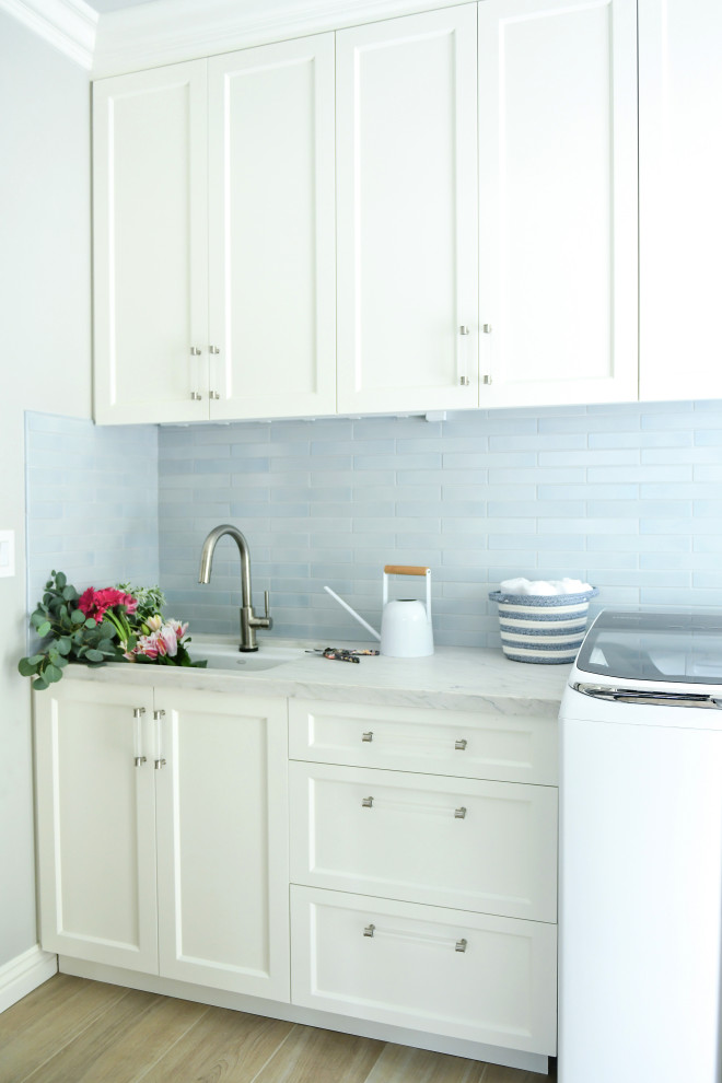 Inspiration for a mid-sized transitional galley dedicated laundry room in San Diego with an undermount sink, shaker cabinets, white cabinets, quartzite benchtops, blue splashback, ceramic splashback, grey walls, porcelain floors, a side-by-side washer and dryer, beige floor and white benchtop.