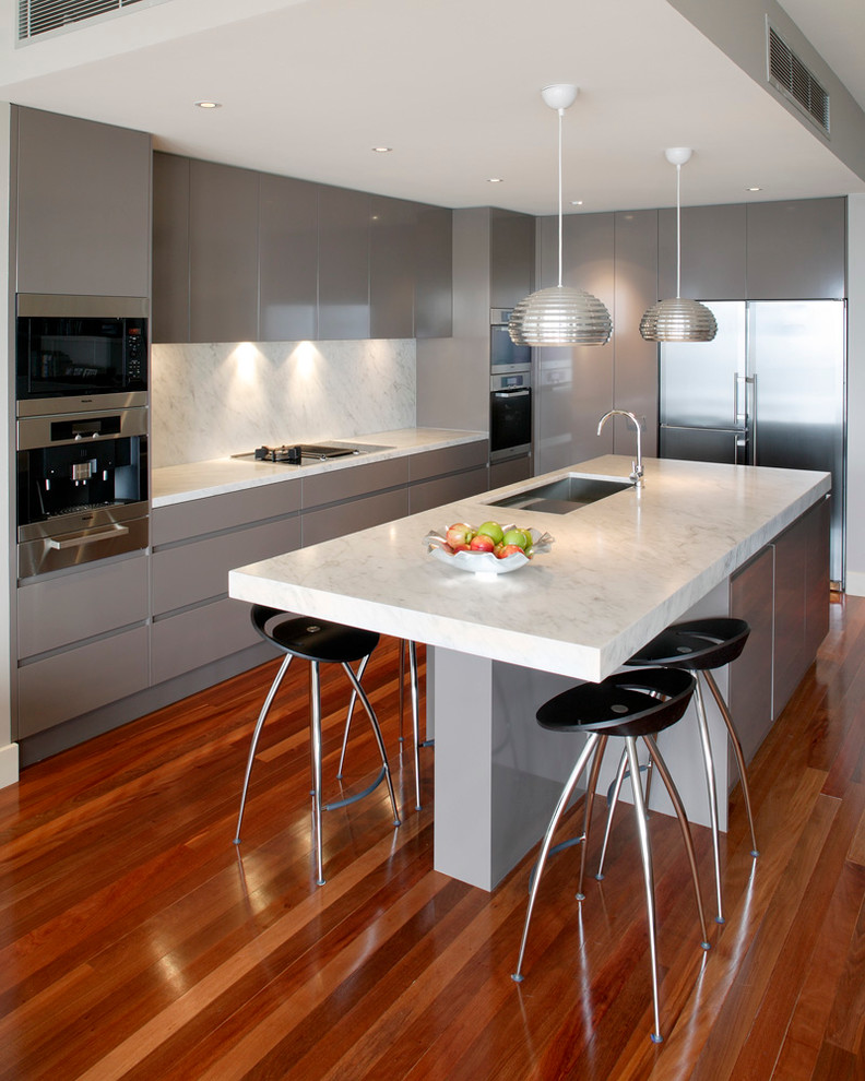 Photo of a mid-sized contemporary l-shaped open plan kitchen in Sydney with an undermount sink, flat-panel cabinets, beige cabinets, marble benchtops, white splashback, stone slab splashback, stainless steel appliances, medium hardwood floors and with island.