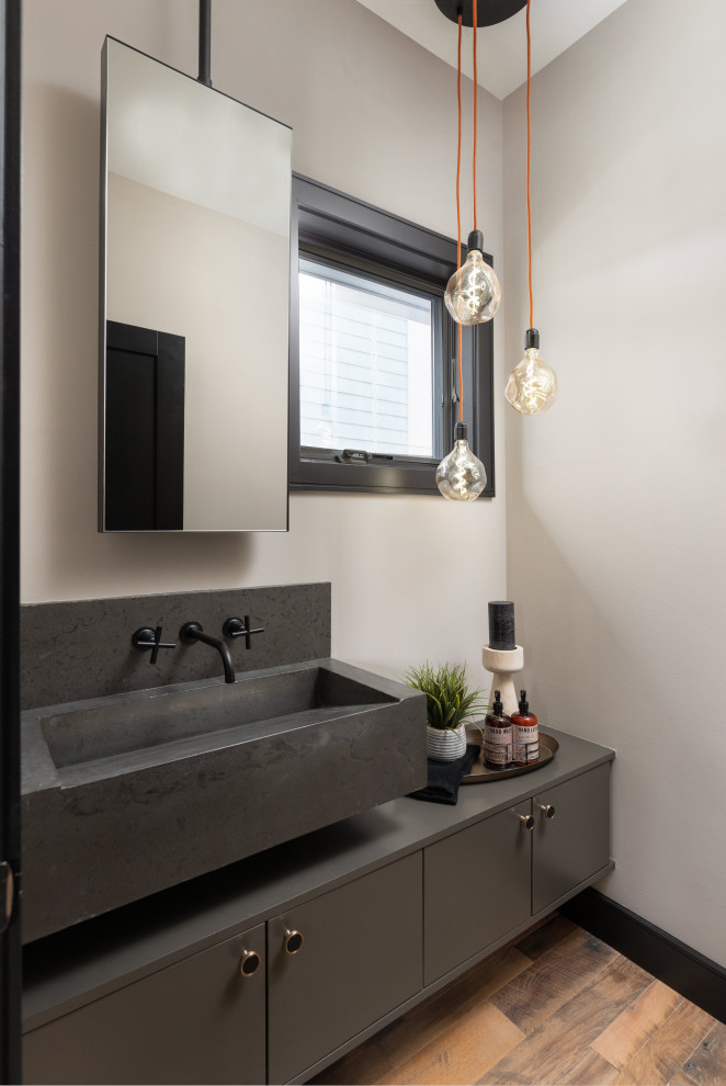 Small contemporary powder room in Detroit with flat-panel cabinets, grey cabinets, a wall-mount toilet, beige walls, medium hardwood floors, a trough sink, concrete benchtops, brown floor, black benchtops and a floating vanity.