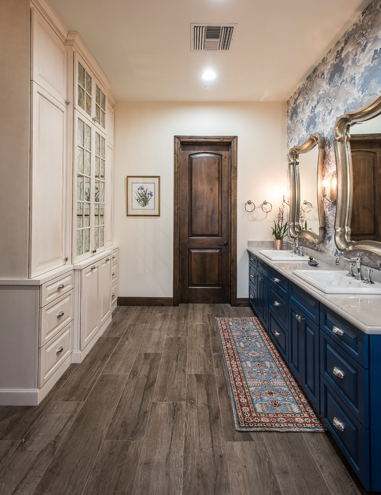 This is an example of a mid-sized country master bathroom in Phoenix with raised-panel cabinets, blue cabinets, multi-coloured walls, vinyl floors, a drop-in sink, brown floor and grey benchtops.