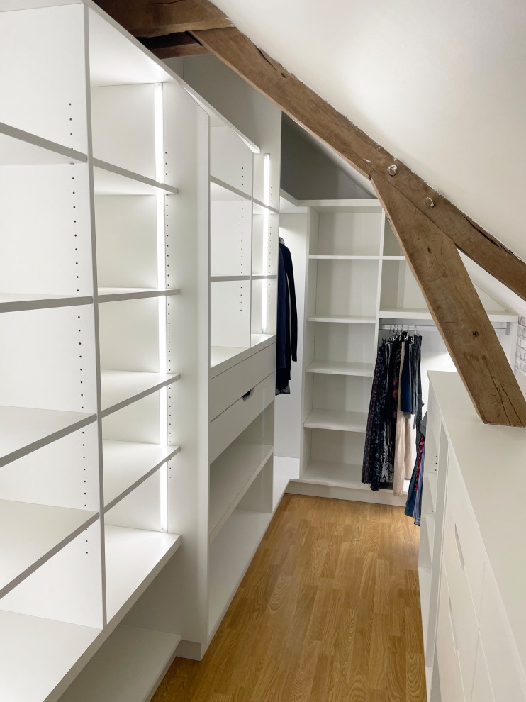 Ejemplo de vestidor unisex clásico renovado de tamaño medio con armarios abiertos, puertas de armario blancas, suelo de madera clara, suelo beige y vigas vistas