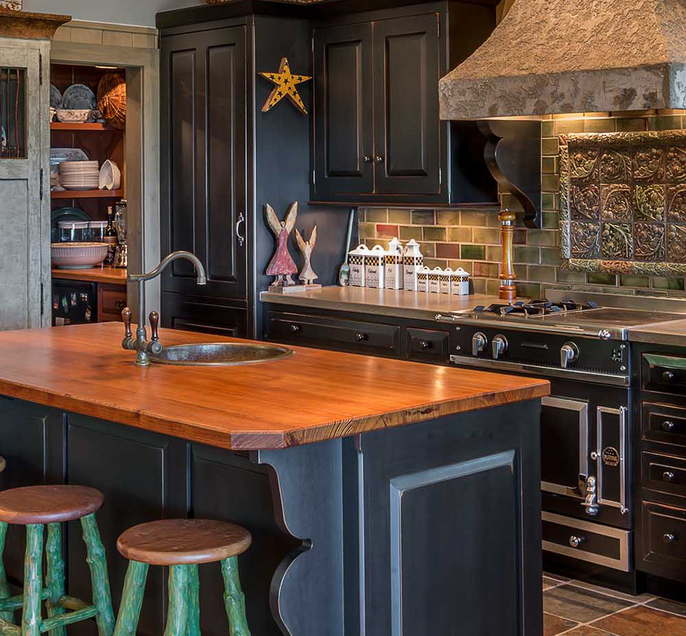 Small country single-wall kitchen in Chicago with black cabinets, wood benchtops, multi-coloured splashback, black appliances, with island, a drop-in sink and raised-panel cabinets.