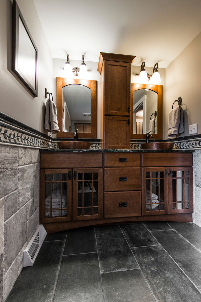 Photo of a large transitional 3/4 bathroom in Milwaukee with shaker cabinets, medium wood cabinets, an alcove tub, a shower/bathtub combo, a two-piece toilet, gray tile, slate, beige walls, slate floors, a vessel sink and granite benchtops.