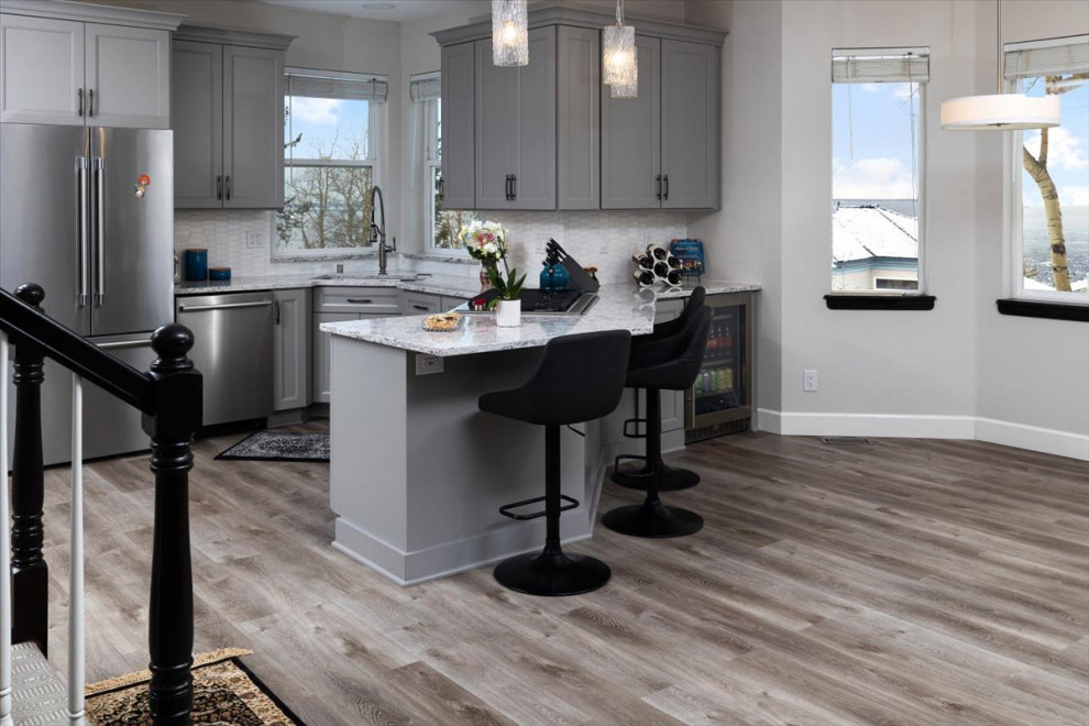 Mid-sized transitional laminate floor and gray floor open concept kitchen photo with recessed-panel cabinets, gray cabinets, quartz countertops, white backsplash, marble backsplash, stainless steel appliances and white countertops