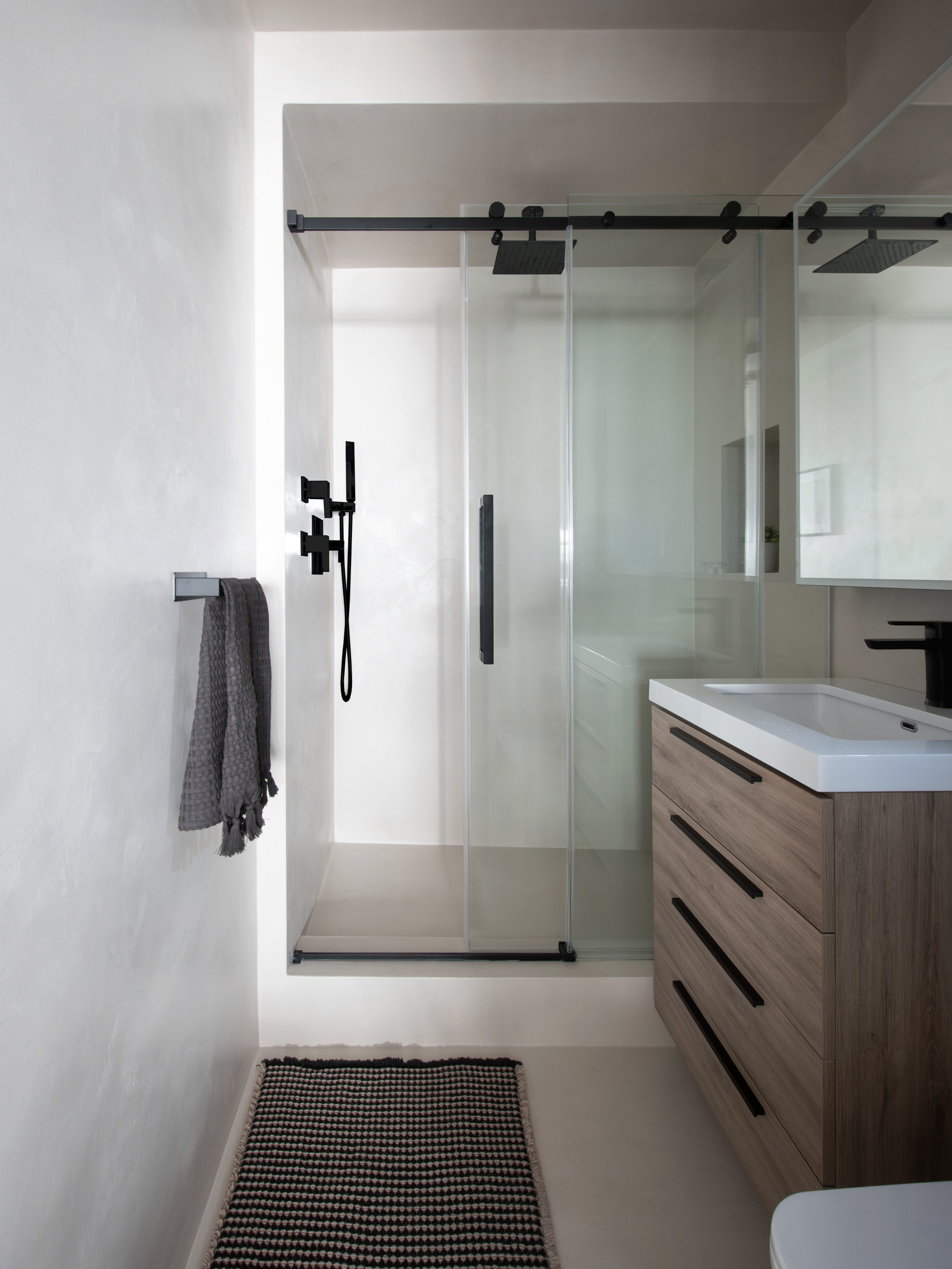 A sleek, modern bathroom renovation in New York City featuring a seamless microcement finish for a clean, grout-free look. This contemporary NYC bathroom design combines minimalist lines, a custom woo