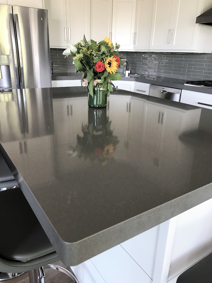 Example of a mid-sized transitional l-shaped light wood floor and gray floor eat-in kitchen design with an undermount sink, recessed-panel cabinets, white cabinets, quartz countertops, gray backsplash, ceramic backsplash, stainless steel appliances and an island