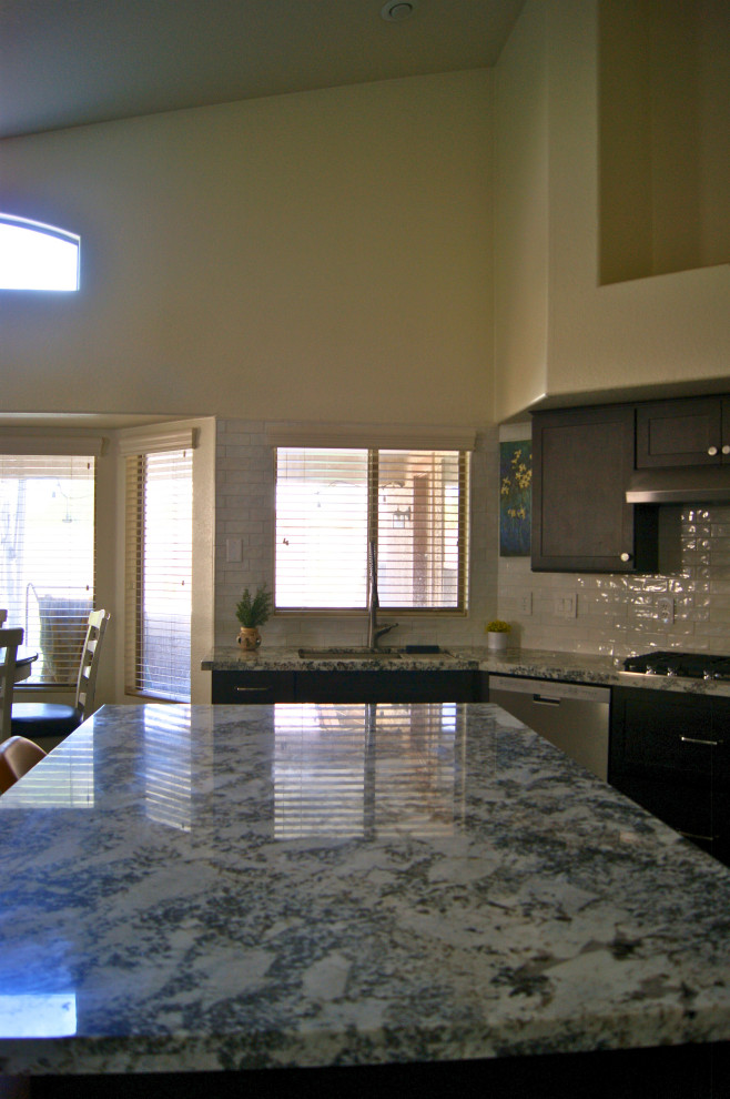 Example of a mid-sized minimalist l-shaped porcelain tile and gray floor open concept kitchen design in Phoenix with an undermount sink, shaker cabinets, brown cabinets, granite countertops, white backsplash, subway tile backsplash, stainless steel appliances, an island and white countertops