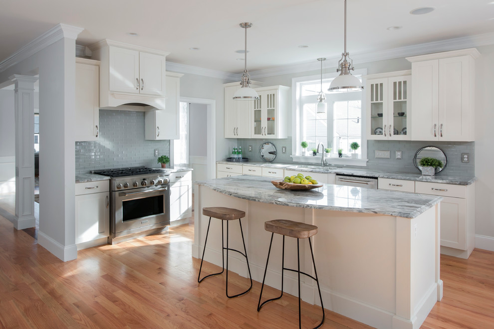 Traditional kitchen in Boston with an undermount sink, shaker cabinets, white cabinets, grey splashback, stainless steel appliances, light hardwood floors and with island.