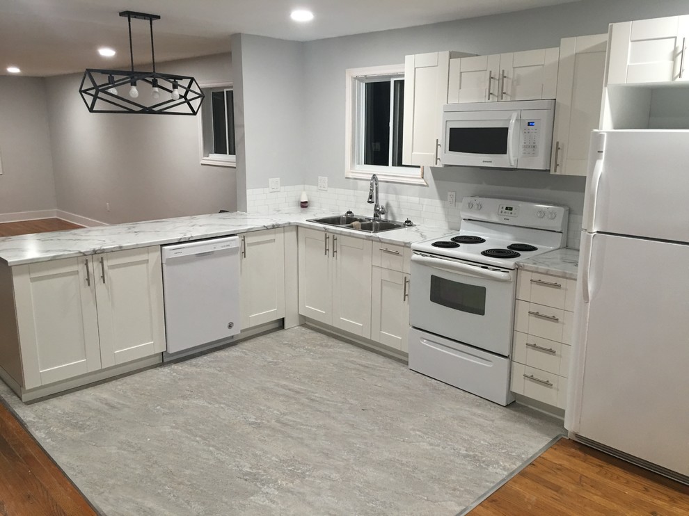 Example of a mid-sized transitional l-shaped vinyl floor and gray floor eat-in kitchen design with a double-bowl sink, shaker cabinets, white cabinets, laminate countertops, white backsplash, subway tile backsplash, white appliances, a peninsula and white countertops