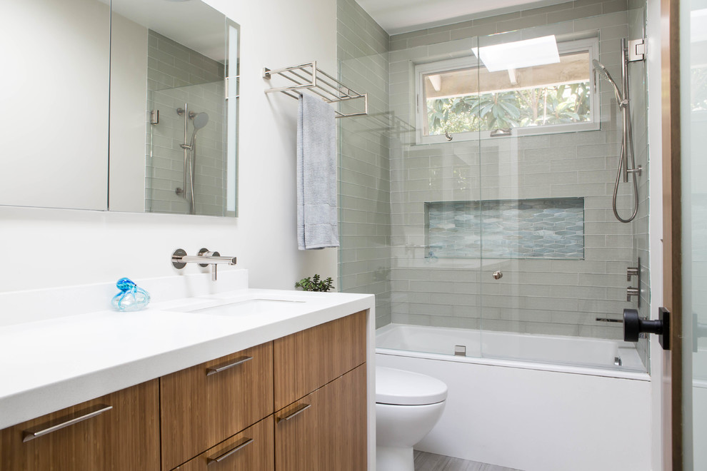 Contemporary 3/4 bathroom in Los Angeles with flat-panel cabinets, medium wood cabinets, an alcove tub, a shower/bathtub combo, glass tile, porcelain floors, an undermount sink, engineered quartz benchtops, grey floor, an open shower and white benchtops.