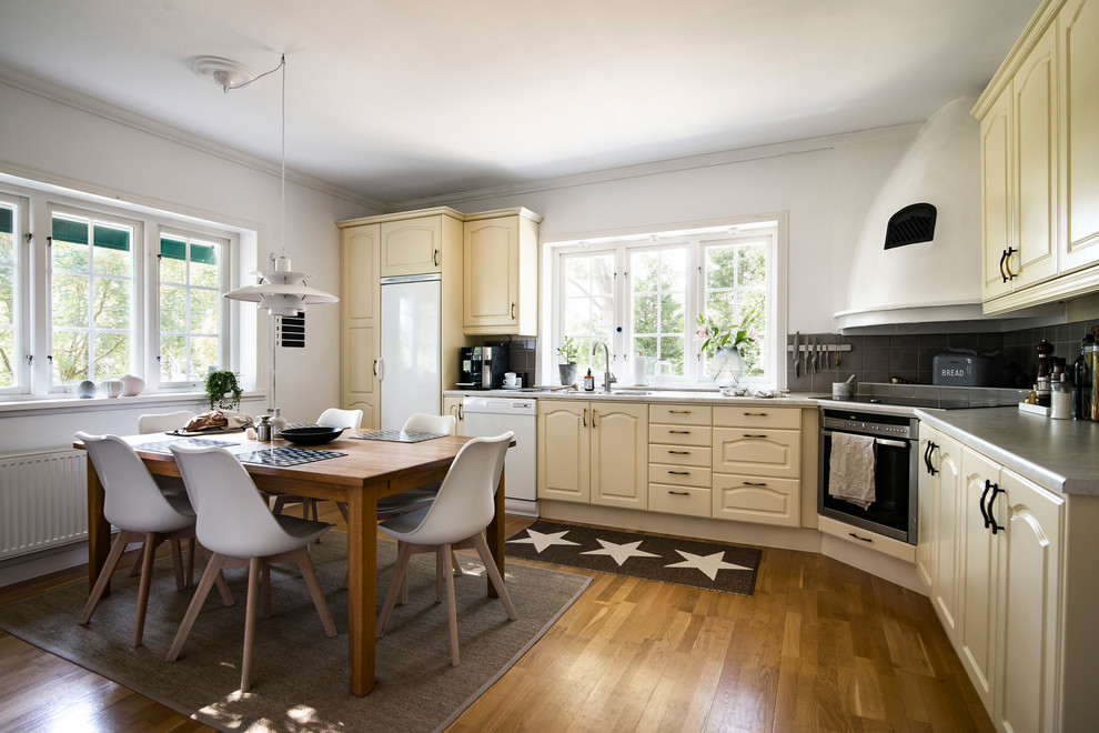 This is an example of a mid-sized scandinavian l-shaped eat-in kitchen in Stockholm with raised-panel cabinets, beige cabinets, grey splashback, medium hardwood floors, no island, brown floor and grey benchtop.