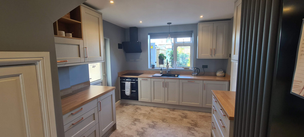 This is an example of a small contemporary galley separate kitchen in West Midlands with a single-bowl sink, shaker cabinets, white cabinets, wood benchtops and white splashback.
