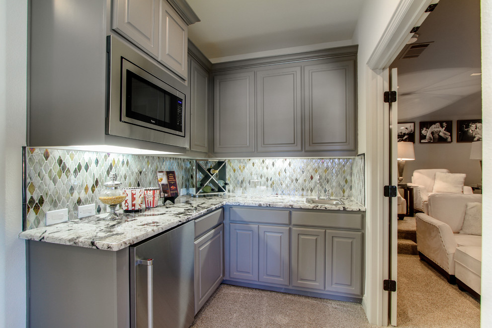 Mid-sized l-shaped wet bar in Dallas with a drop-in sink, raised-panel cabinets, grey cabinets, granite benchtops, multi-coloured splashback, glass tile splashback and carpet.