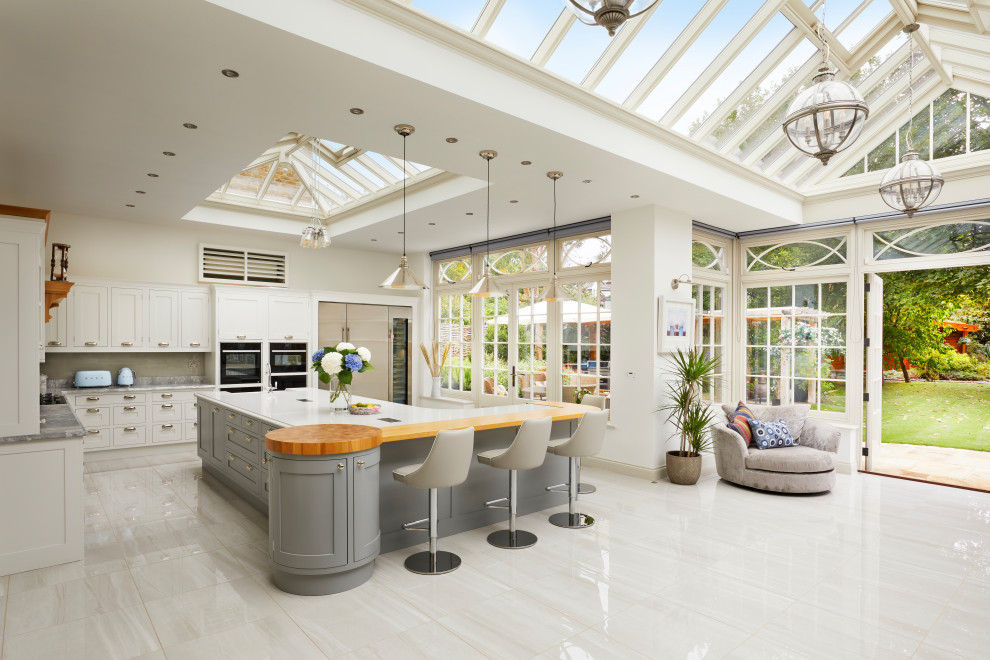 This is an example of a large transitional u-shaped open plan kitchen in Essex with an undermount sink, recessed-panel cabinets, white cabinets, marble benchtops, grey splashback, marble splashback, stainless steel appliances, marble floors, a peninsula, white floor, grey benchtop and vaulted.