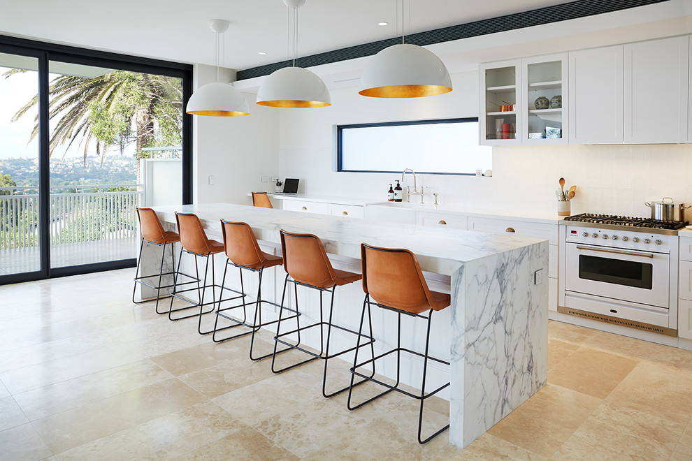Inspiration for a large contemporary single-wall kitchen in Sydney with a farmhouse sink, shaker cabinets, white cabinets, white splashback, white appliances, travertine floors and with island.