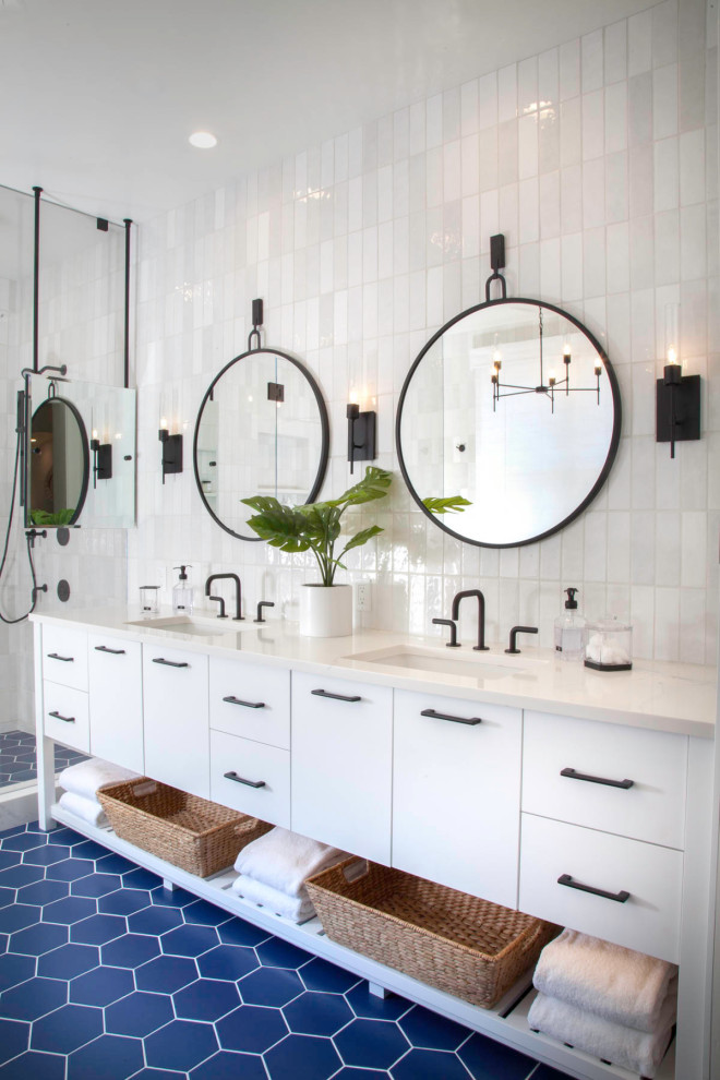 Photo of a large beach style master bathroom in San Diego with flat-panel cabinets, white cabinets, a freestanding tub, a double shower, a one-piece toilet, white tile, ceramic tile, white walls, porcelain floors, an undermount sink, engineered quartz benchtops, blue floor, a hinged shower door, white benchtops, a niche, a double vanity and a freestanding vanity.