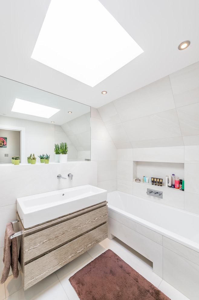 Design ideas for a contemporary bathroom in London with flat-panel cabinets, light wood cabinets, an alcove tub, white tile, white walls and an integrated sink.