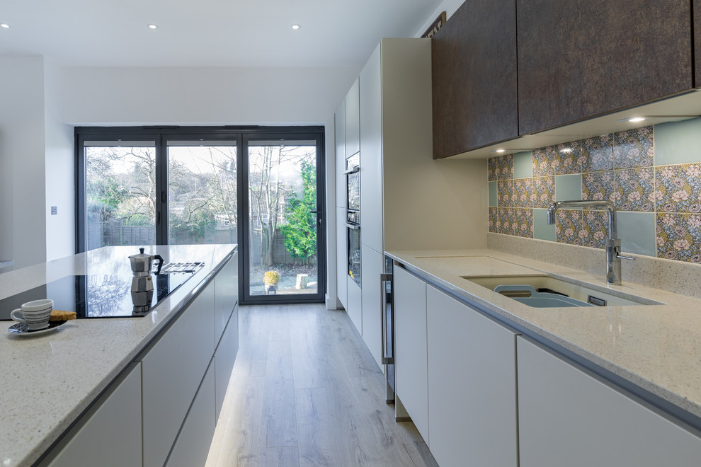 Photo of a mid-sized modern single-wall open plan kitchen in Hampshire with an undermount sink, flat-panel cabinets, white cabinets, quartzite benchtops, metallic splashback, panelled appliances, light hardwood floors and with island.