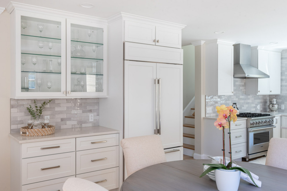 Open concept kitchen - huge transitional l-shaped light wood floor and brown floor open concept kitchen idea in Boston with an undermount sink, shaker cabinets, white cabinets, quartz countertops, gray backsplash, subway tile backsplash, stainless steel appliances, an island and white countertops