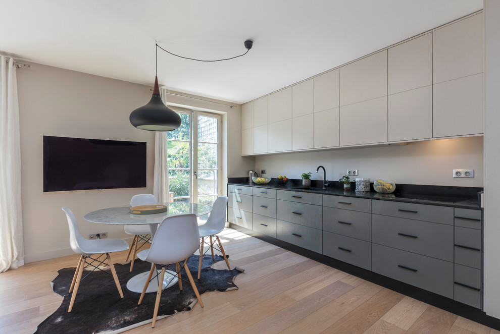 Photo of a mid-sized contemporary single-wall open plan kitchen in Paris with an integrated sink, beaded inset cabinets, beige cabinets, granite benchtops, black splashback, stone slab splashback, panelled appliances, light hardwood floors, no island, beige floor and black benchtop.