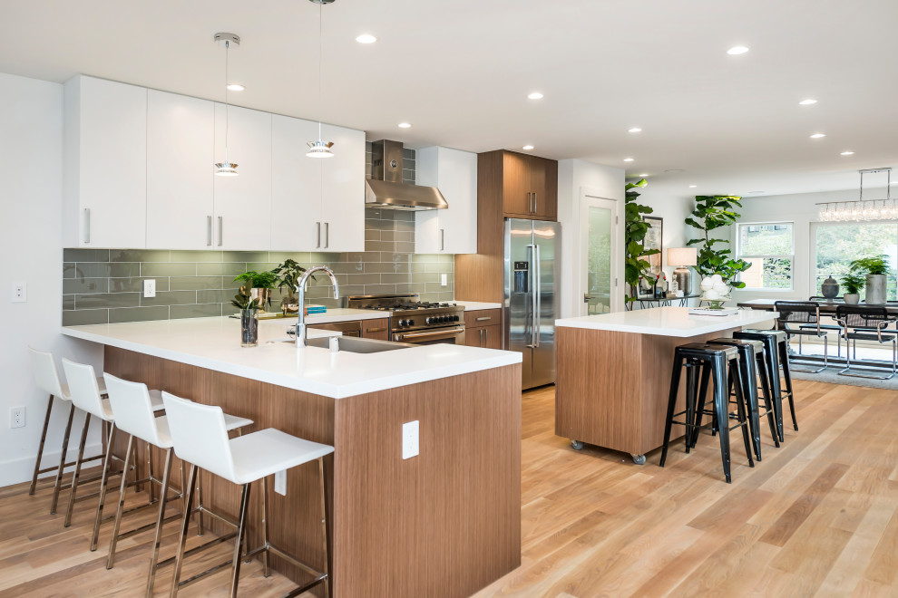 Trendy l-shaped light wood floor and beige floor kitchen photo in Other with a farmhouse sink, flat-panel cabinets, medium tone wood cabinets, green backsplash, glass tile backsplash, stainless steel appliances, an island and white countertops