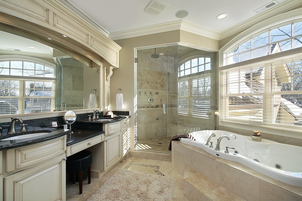Photo of a bathroom in New York with an undermount sink, furniture-like cabinets, beige cabinets, marble benchtops, a drop-in tub, a corner shower and beige tile.