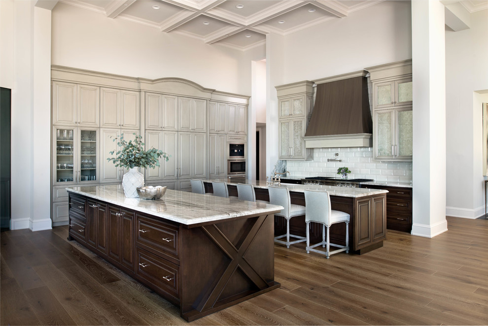 Inspiration for an expansive transitional l-shaped open plan kitchen in Miami with a farmhouse sink, raised-panel cabinets, dark wood cabinets, white splashback, subway tile splashback, stainless steel appliances, multiple islands, brown floor, grey benchtop, coffered, quartzite benchtops and medium hardwood floors.