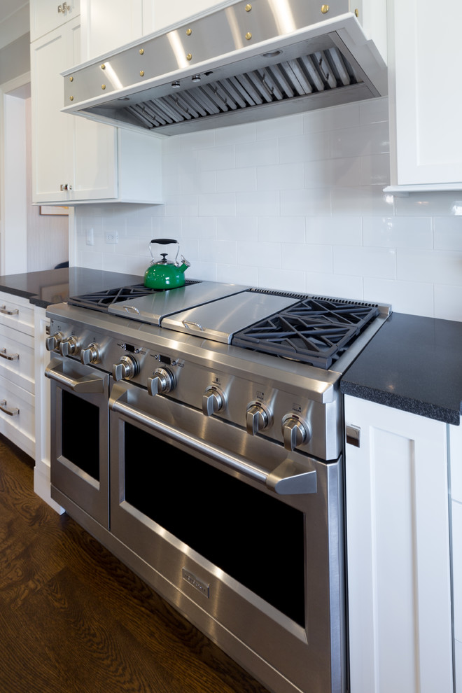 Large transitional u-shaped dark wood floor and brown floor kitchen photo in Chicago with an undermount sink, shaker cabinets, white cabinets, solid surface countertops, white backsplash, ceramic backsplash, stainless steel appliances, an island and black countertops