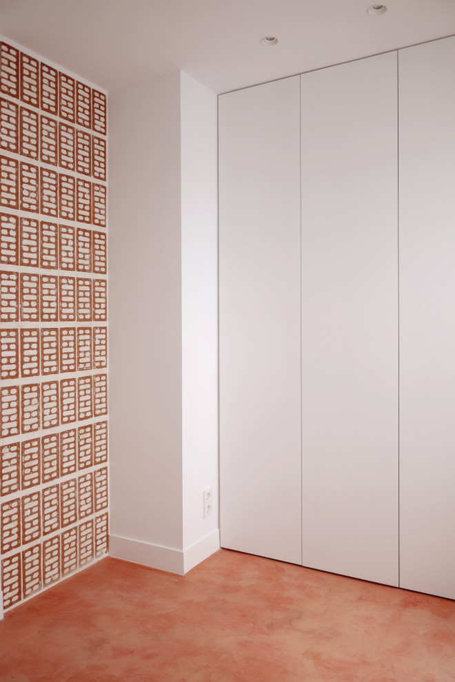 Ejemplo de armario y vestidor unisex minimalista pequeño con a medida, armarios con paneles lisos, puertas de armario blancas, suelo de cemento y suelo rojo