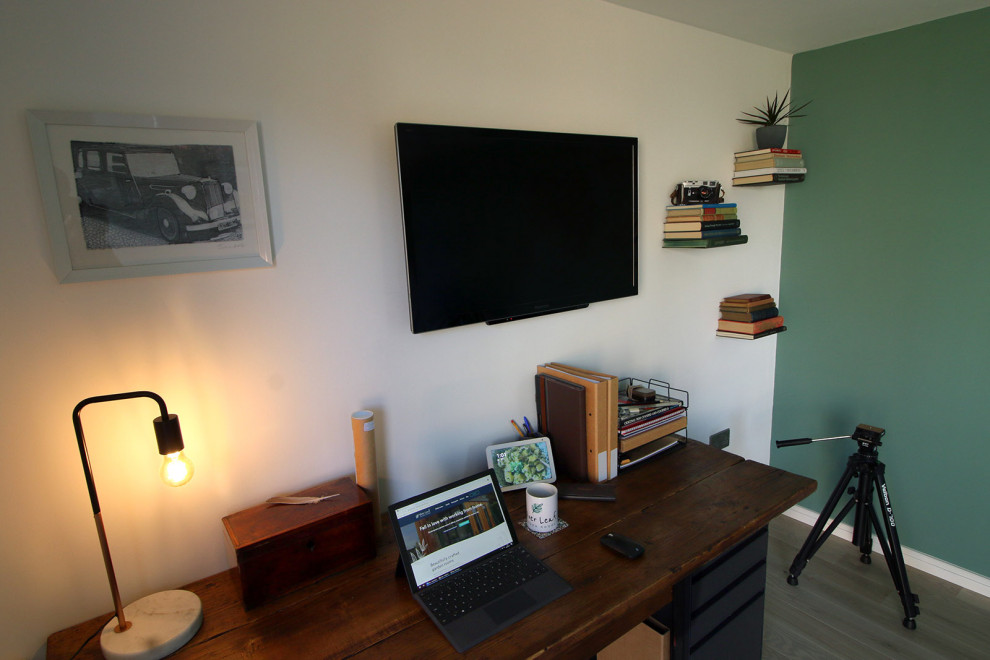 This is an example of a mid-sized contemporary home studio in Surrey with green walls, light hardwood floors, a freestanding desk and brown floor.
